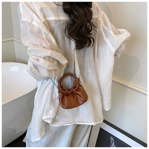 Brown pleated mini bag with metal chain strap worn by model in minimalist setting