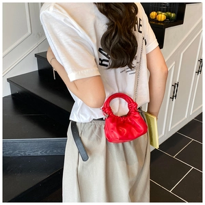 Detail of red pleated PU leather handbag with metallic chain strap and round handle