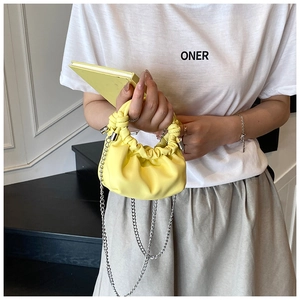 Detail of a bright yellow pleated dumpling bag with knot handle and silver chain strap