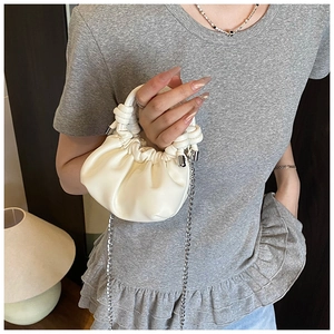 Close-up of white pleated cloud bag featuring woven handle and silver chain strap