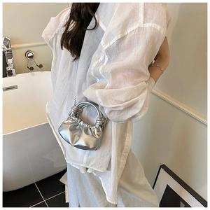 Close-up of metallic silver pleated cloud bag with braided handle and chain strap on model