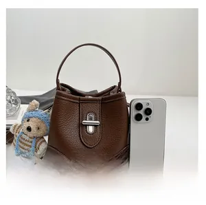 Detail of dark brown pebble leather bucket bag with silver lock and size reference phone
