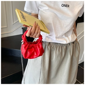 Close-up of a red pleated mini pouch bag with twisted handle and metal chain strap
