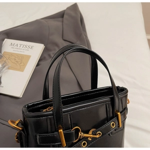 Detail of black leather bucket bag with vertical stitching and polished gold hardware