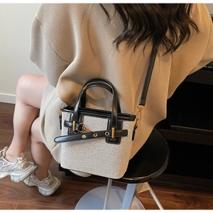 Detail of a two-tone canvas tote with leather trim and gold chain hardware worn by a model