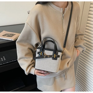 Detail of beige canvas and black leather crossbody bag with golden buckle on model