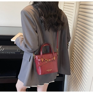 Detail of burgundy leather mini bucket bag with gold buckle and crossbody strap on grey blazer