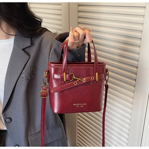 Detail of burgundy bucket bag with glossy leather, gold hardware and Maven Chic logo