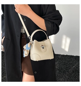 Detail of beige bucket bag with silver clasp, bear charm, and crossbody styling