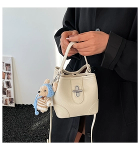 Detail of cream white bucket bag with pebble leather texture and cute bear charm