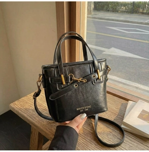 Close-up of black leather bucket bag with gold buckle and embossed logo on wood bench