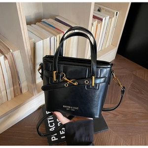 Detail of black leather bucket bag featuring gold hardware and logo on a wooden shelf