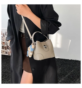 Detail of grey lychee leather handbag with silver lock and a cute teddy bear charm