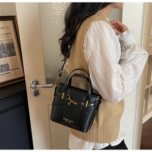 Side view of black glossy leather bucket bag with gold buckle and adjustable strap
