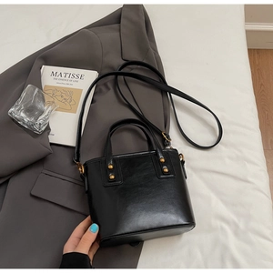 Close-up of black leather bucket bag with gold rivets on a white bedding backdrop