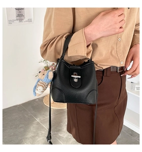 Detail of black pebbled leather bucket bag with silver lock and a cute bear charm