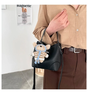 Detail of black lychee grain leather bucket bag featuring a cute teddy bear charm