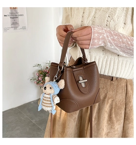 Detail of dark brown lychee leather bucket bag with clasp and cute teddy bear charm
