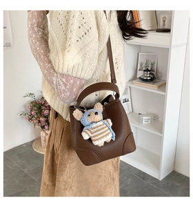 Detailed shot of brown litchi grain leather bucket bag with cute plush bear charm accessory