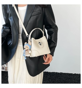 Detail view of cream bucket bag with cute bear charm and thin shoulder strap shown on model