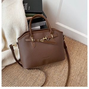 Detail of a brown lychee pattern leather handbag featuring gold metal buckle and strap