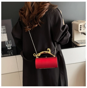 Detail of red cylindrical velvet evening bag featuring a gold leopard handle and chain