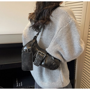 Detail of black leather underarm bag with metal buckles and mini pouch on model