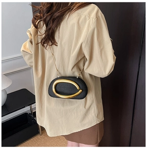 Detailed view of black evening bag featuring a bold gold oval metal ring and fine chain strap