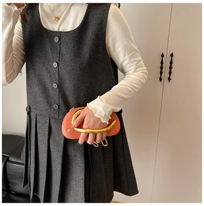 Detailed shot of an orange oval clutch bag with a bold gold semi-circular metal handle
