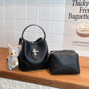 Litchi pattern bucket bag in black with silver twist lock and bear charm on wooden desk