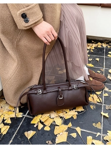 Detail of dark brown baguette bag with silver buckles on autumn ginkgo leaves background