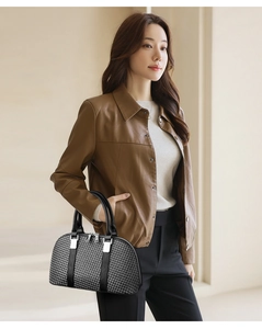Detail of black woven texture handbag with silver metal buckles on brown leather coat