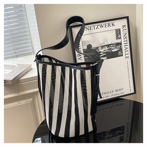 Detail of striped mesh bucket bag with black leather straps on a reflective desk