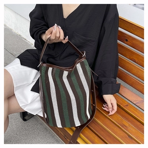 Detail of striped mesh bucket bag with leather handles shown on a wooden bench