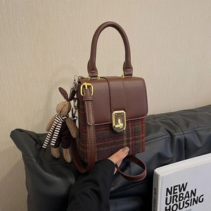 Detail of vintage plaid messenger bag with brown leather trim and cute rabbit charm
