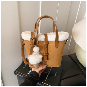 Close-up of brown suede bucket bag featuring a white faux fur trim and fluffy ball charm