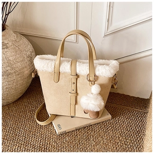 Detail of beige faux suede handbag with white fur trim and plush ball charm on a magazine