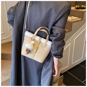 Detail of faux fur trim and plush ball pendant on a beige crossbody tote bag
