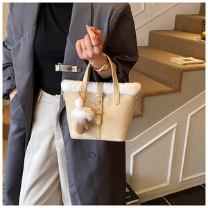 Detail of a beige faux suede bucket bag featuring white plush trim and a heart charm