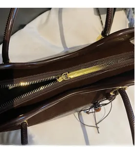 Detail of a smooth golden zipper and premium leather texture on a dark brown tote bag