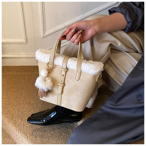 Close-up of beige faux suede handbag with plush white fur trim and decorative pom pom