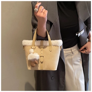 Close-up of beige plush bucket bag with white faux fur trim and furry ball pendant