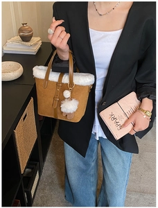 Detail of suede tote bag with faux fur trim and fluffy ball charm held by model