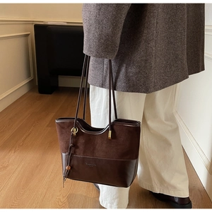 Detail of dark brown tote bag showing textured contrast stitching and decorative tassel