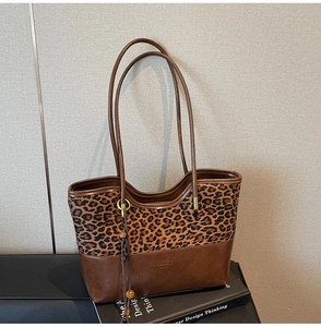 Detail of leopard print tote bag with brown leather trim and beaded tassel charm