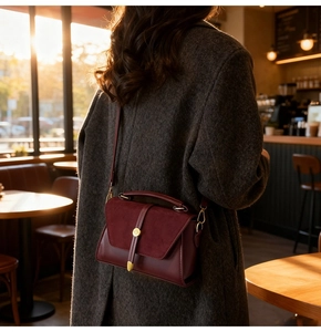 Dettaglio borsa in pelle bordeaux con chiusura dorata indossata su cappotto grigio