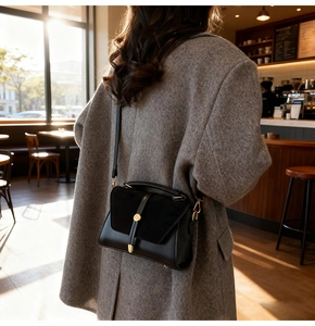 Borsa a tracolla nera opaca con anello dorato mostrata in un ambiente di caffè
