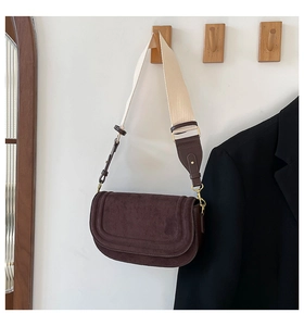 Detail of brown suede saddle bag with gold buckle and cream wide shoulder strap