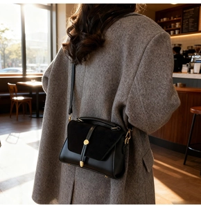 Dettaglio di una borsa a tracolla nera opaca con hardware dorato su un cappotto grigio