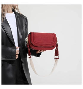 Detail of red suede crossbody bag with wide woven strap and gold hardware accents
